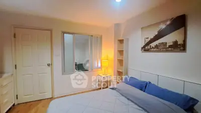 Cozy bedroom with modern decor and warm lighting, featuring a cityscape artwork and ample storage.