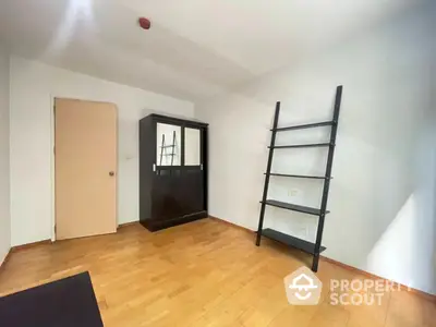 Minimalist bedroom with wooden flooring, sleek black wardrobe, and modern ladder-style shelf.