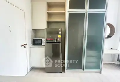 Modern compact kitchen with stainless steel fridge and microwave in sleek apartment