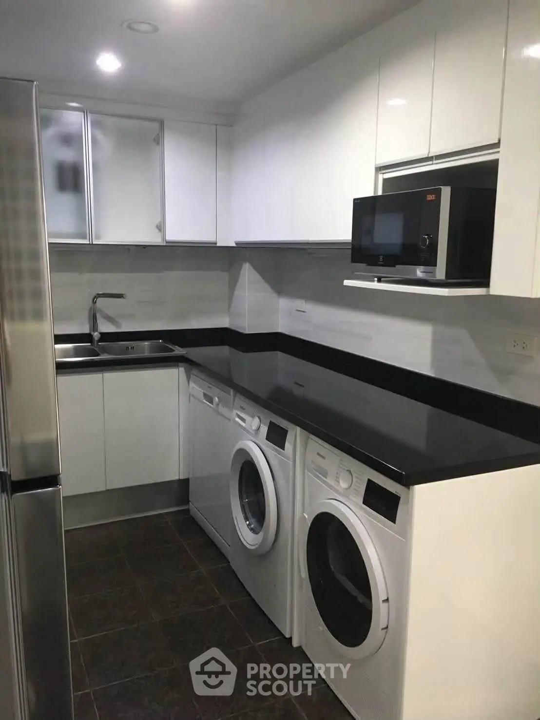 Modern kitchen with sleek appliances and black countertops, featuring washing machine and microwave.