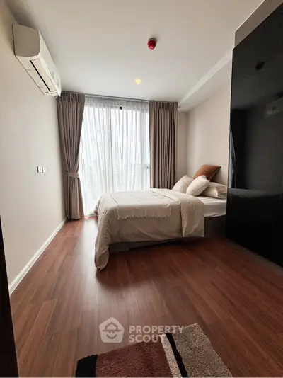 Cozy bedroom with wooden flooring and large window for natural light