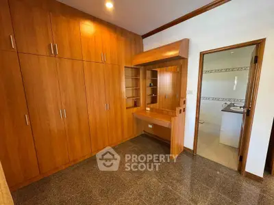 Spacious bedroom with built-in wooden wardrobe and vanity, adjacent to a bathroom.