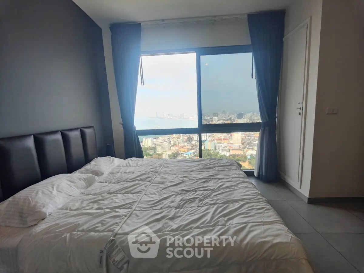 Spacious bedroom with stunning city and sea view from large window, featuring modern decor and cozy ambiance.