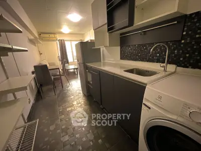 Modern kitchen with sleek cabinetry, washing machine, and dining area in open layout apartment.