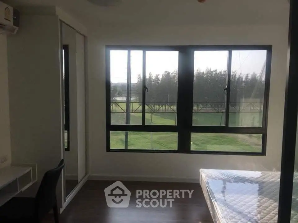 Bright bedroom with large windows offering scenic views of greenery, featuring a comfortable bed and study desk.