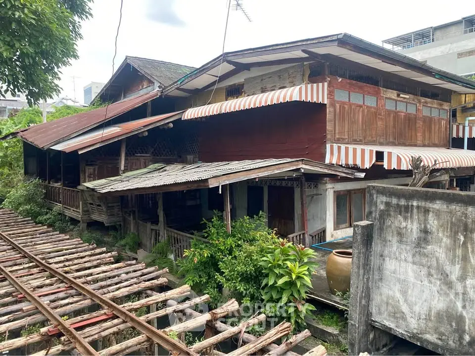 Charming rustic wooden house with striped awnings near railway tracks, lush greenery surrounds.
