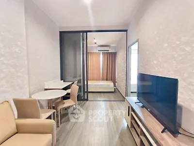 Modern apartment interior with open living and bedroom space, featuring sleek furniture and a large TV.