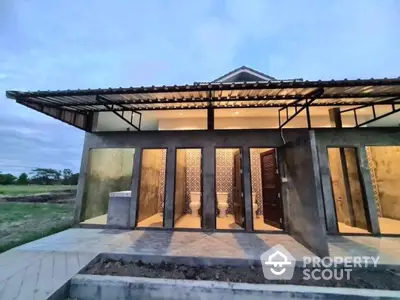 Modern single-story home at dusk featuring expansive glass doors, sleek design, and a welcoming entrance, set against a tranquil natural backdrop.