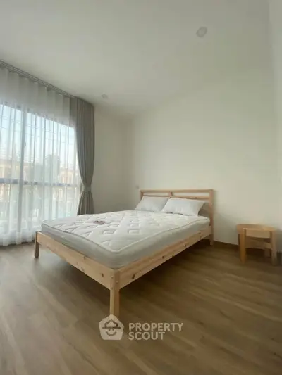 Spacious bedroom with wooden flooring and large window for natural light