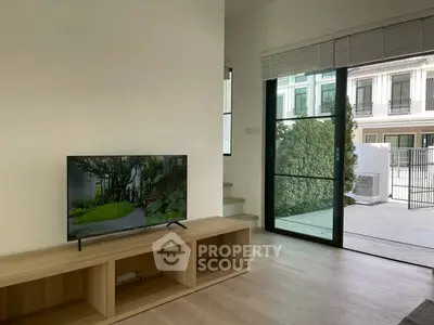 Modern living room with sleek TV stand and large glass doors opening to a garden view.