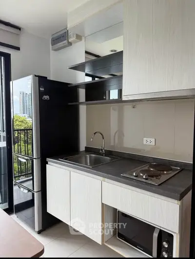 Modern kitchen with sleek cabinets, electric stove, and balcony view in urban apartment.