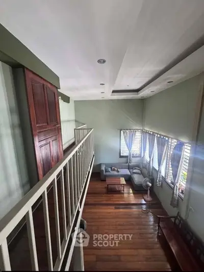Spacious living room with high ceiling and wooden flooring, featuring cozy seating and natural light.