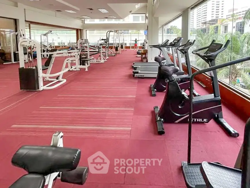 Spacious gym with modern equipment and large windows offering city views.