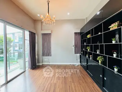 Spacious living room with elegant chandelier and large windows overlooking garden view.