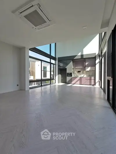 Spacious modern living room with large windows and sleek kitchen area, perfect for contemporary living.