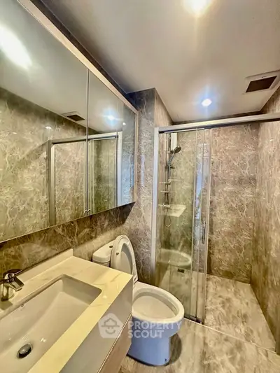 Luxurious modern bathroom with marble finishes and glass shower enclosure.