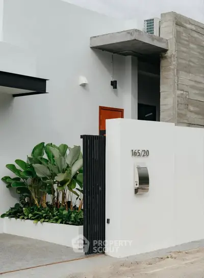 Modern minimalist house entrance with sleek design and lush greenery.
