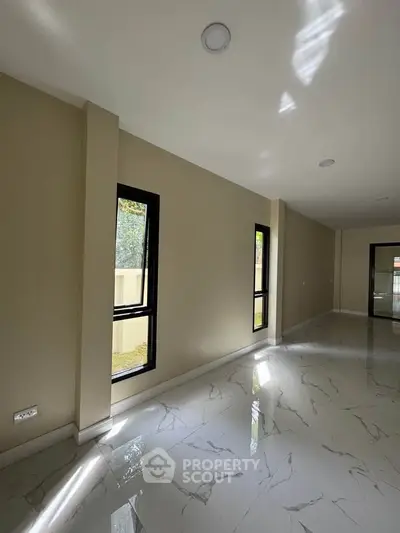 Spacious modern living room with large windows and glossy tiled flooring, offering ample natural light.