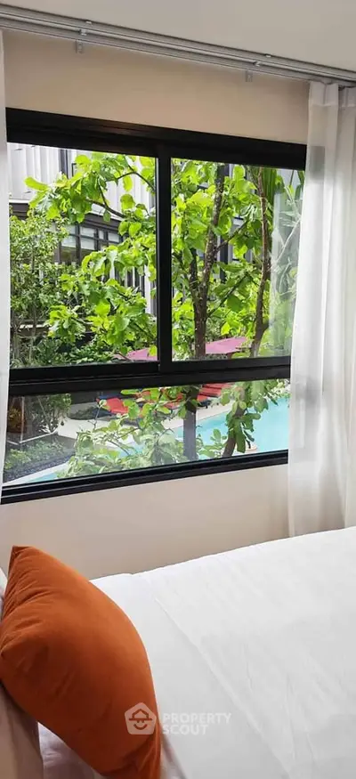 Bright bedroom with pool view through large window, featuring lush greenery and modern design.