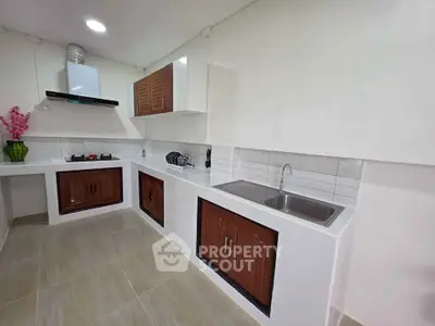 Modern kitchen with sleek white countertops and wooden cabinets, featuring a gas stove and stainless steel sink.