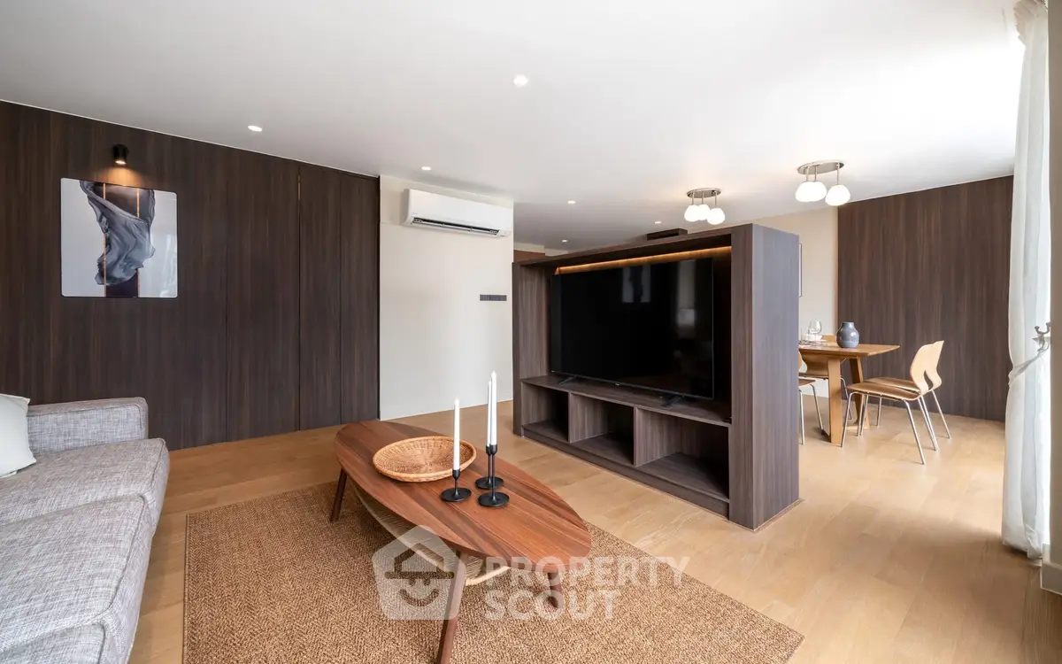 Spacious modern living room with wooden accents and open dining area, featuring a large TV and stylish furniture.