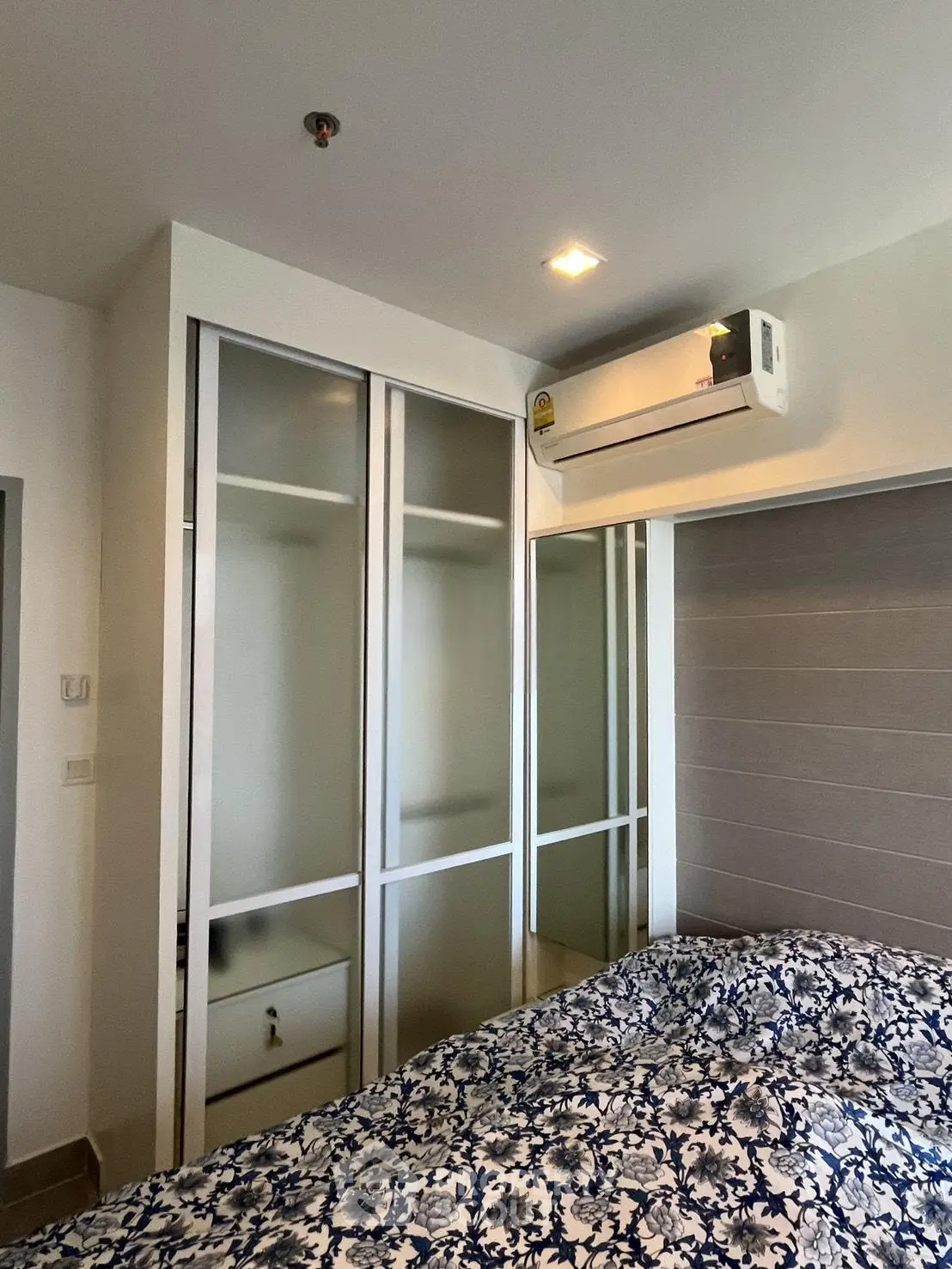 Modern bedroom with built-in wardrobe and air conditioning unit, featuring stylish bedding.
