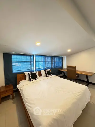 Spacious bedroom with modern decor and natural light, featuring a comfortable bed and work desk.