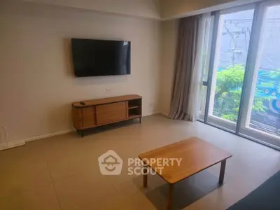 Modern living room with wall-mounted TV and large windows offering natural light.