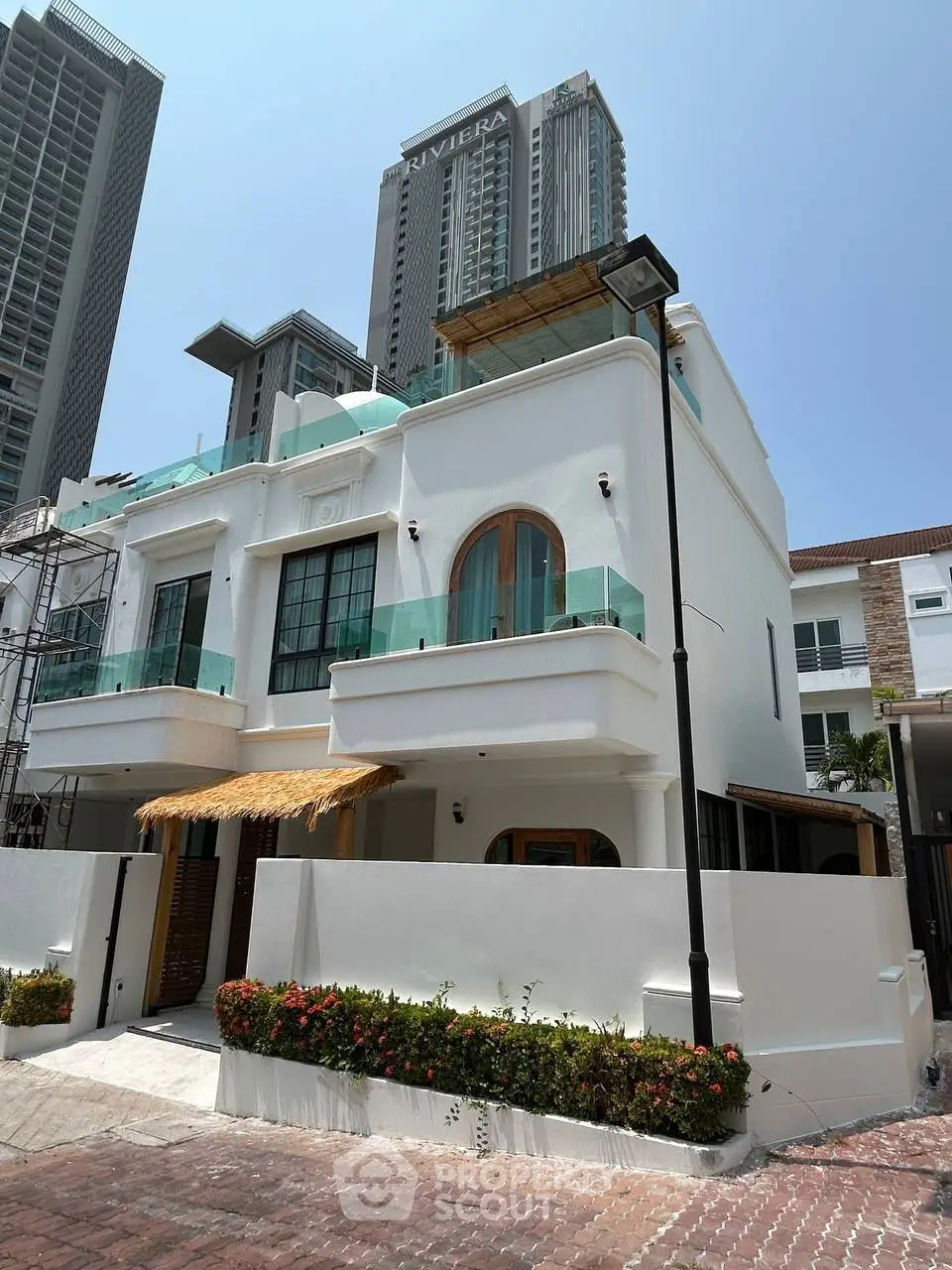 Charming white villa with modern glass balconies and lush greenery, nestled in a vibrant urban setting.