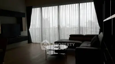 Modern living room with large windows and city view, featuring sleek furniture and natural light.