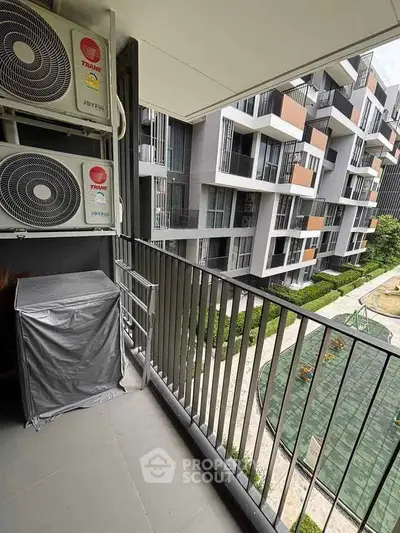 Modern apartment balcony with air conditioning units overlooking a landscaped courtyard.