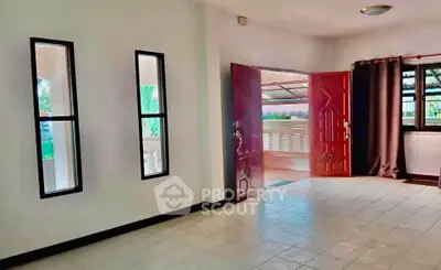 Spacious living room with large windows and elegant red door, perfect for natural light.