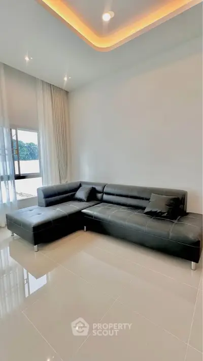 Modern living room with sleek black leather sectional sofa and large windows offering natural light.
