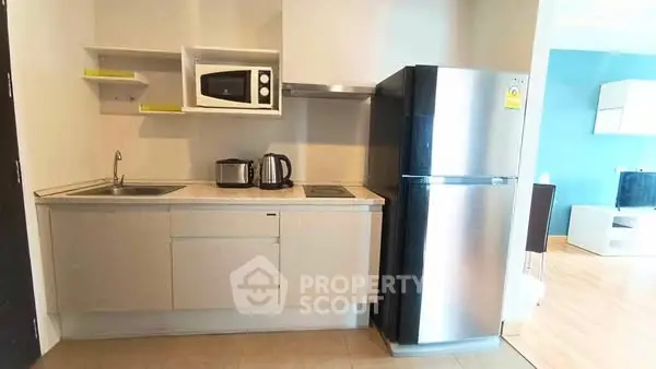 Modern compact kitchen with microwave and stainless steel fridge in cozy apartment.