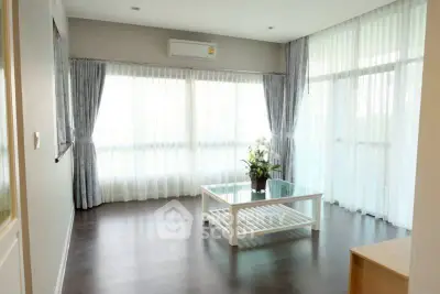 Spacious living room with large windows and elegant curtains, featuring a modern glass coffee table.