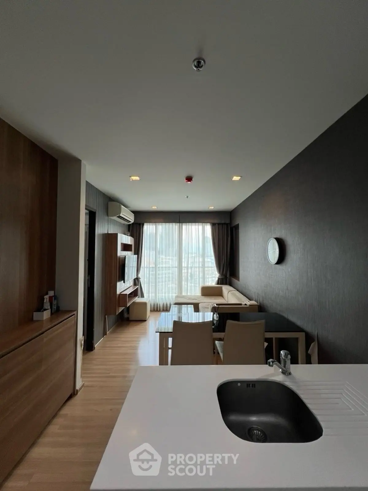 Modern living room with open kitchen, featuring sleek furniture and large windows for natural light.