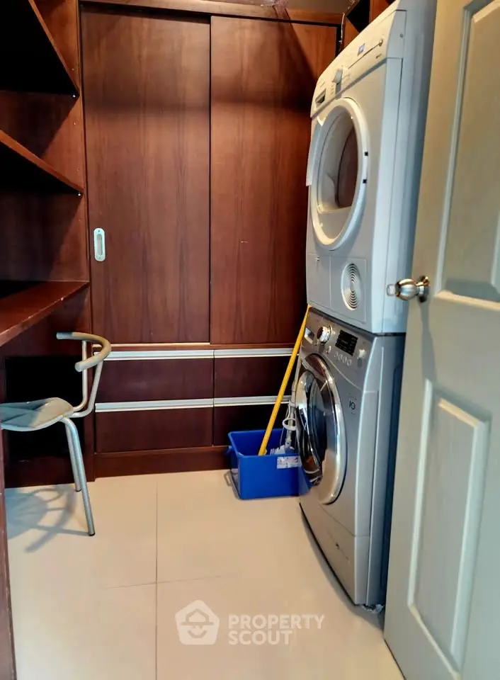 Modern laundry room with stacked washer and dryer, wooden cabinets, and cleaning supplies.
