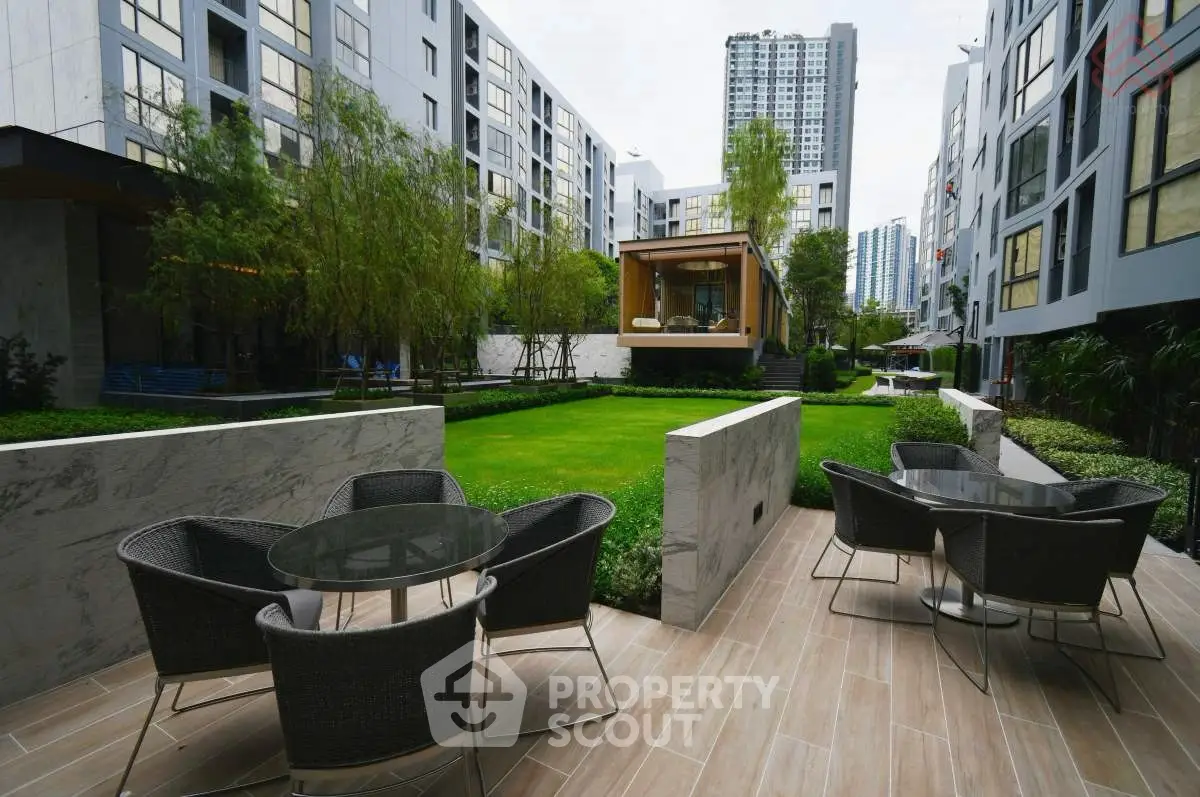 Modern apartment complex with lush garden and outdoor seating area.