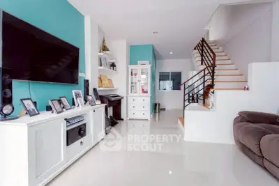 Spacious modern living room with sleek white furniture and large TV, featuring a stylish staircase.