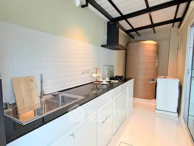 Modern kitchen with sleek countertops and gas stove, featuring a washing machine and large water tank.