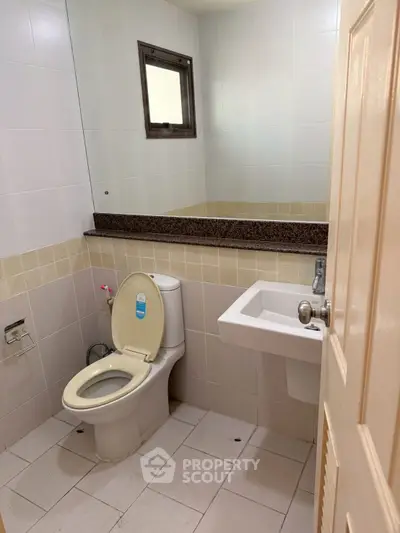 Compact bathroom with toilet, sink, and large mirror in modern apartment.