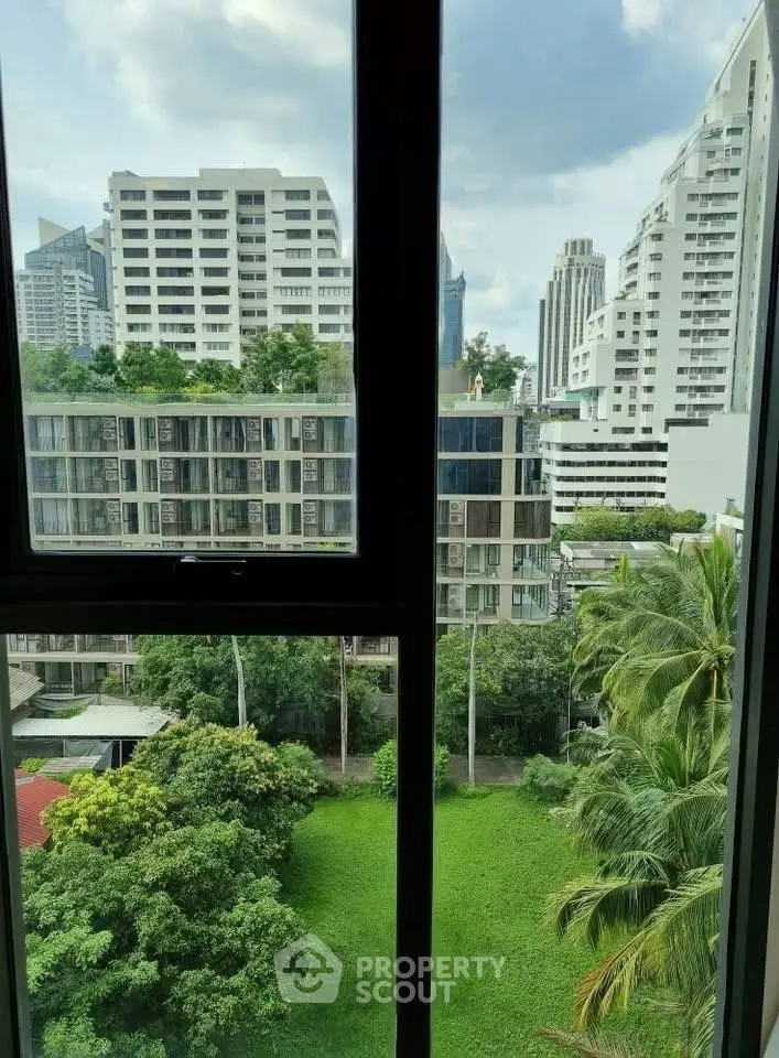 Stunning urban view from a high-rise window overlooking lush greenery and modern buildings.