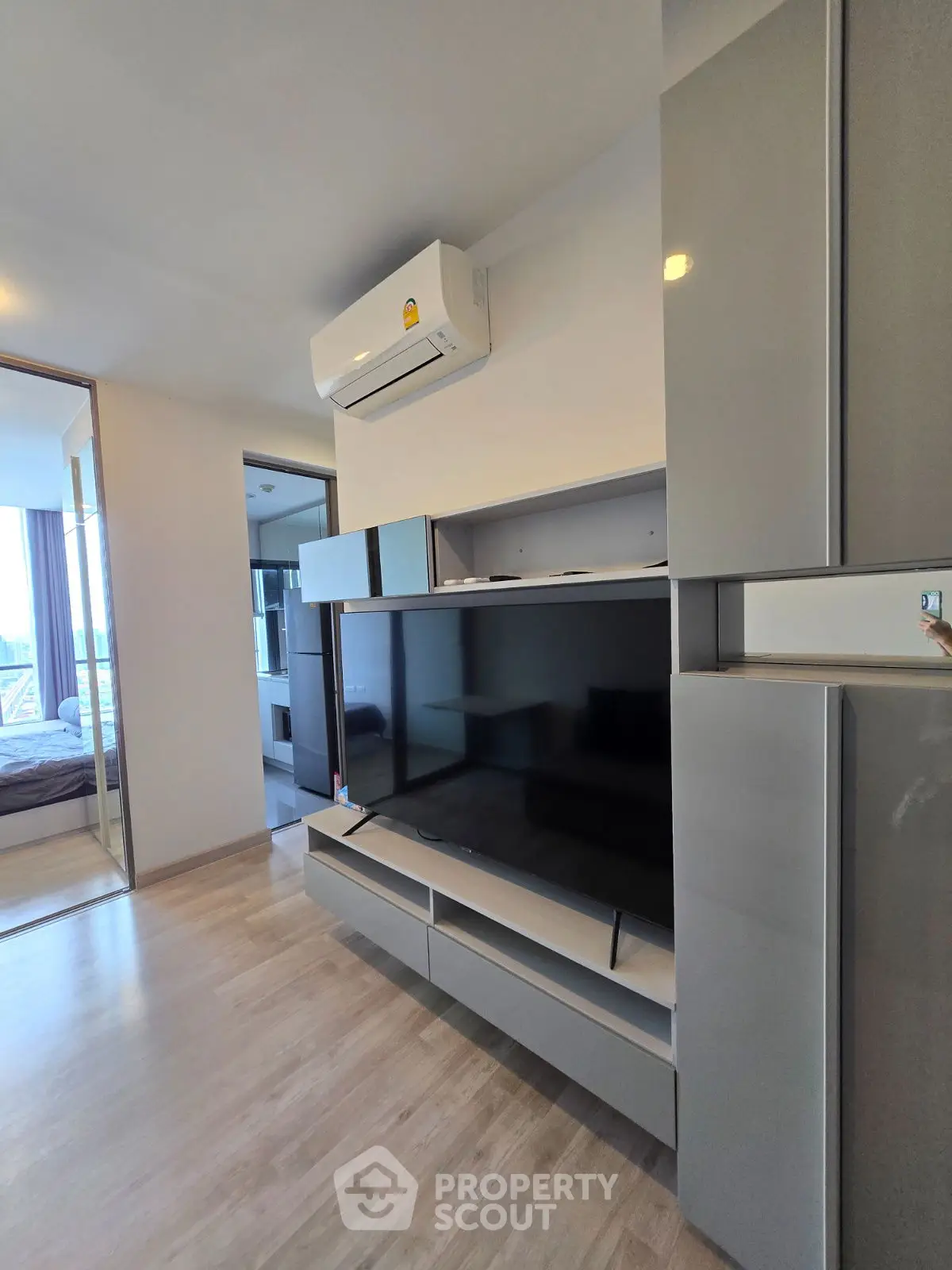 Modern living room with sleek TV unit and air conditioning, featuring a glimpse into a cozy bedroom.