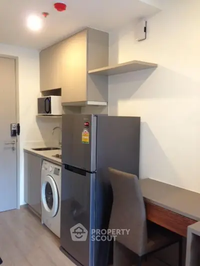 Modern compact kitchen with fridge, washing machine, and microwave in sleek apartment.