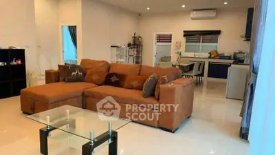 Spacious living room with modern kitchen in open layout, featuring a cozy brown sofa and glass coffee table.