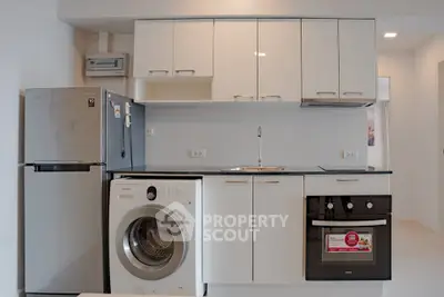 Modern kitchen with sleek cabinets, stainless steel fridge, washing machine, and built-in oven.