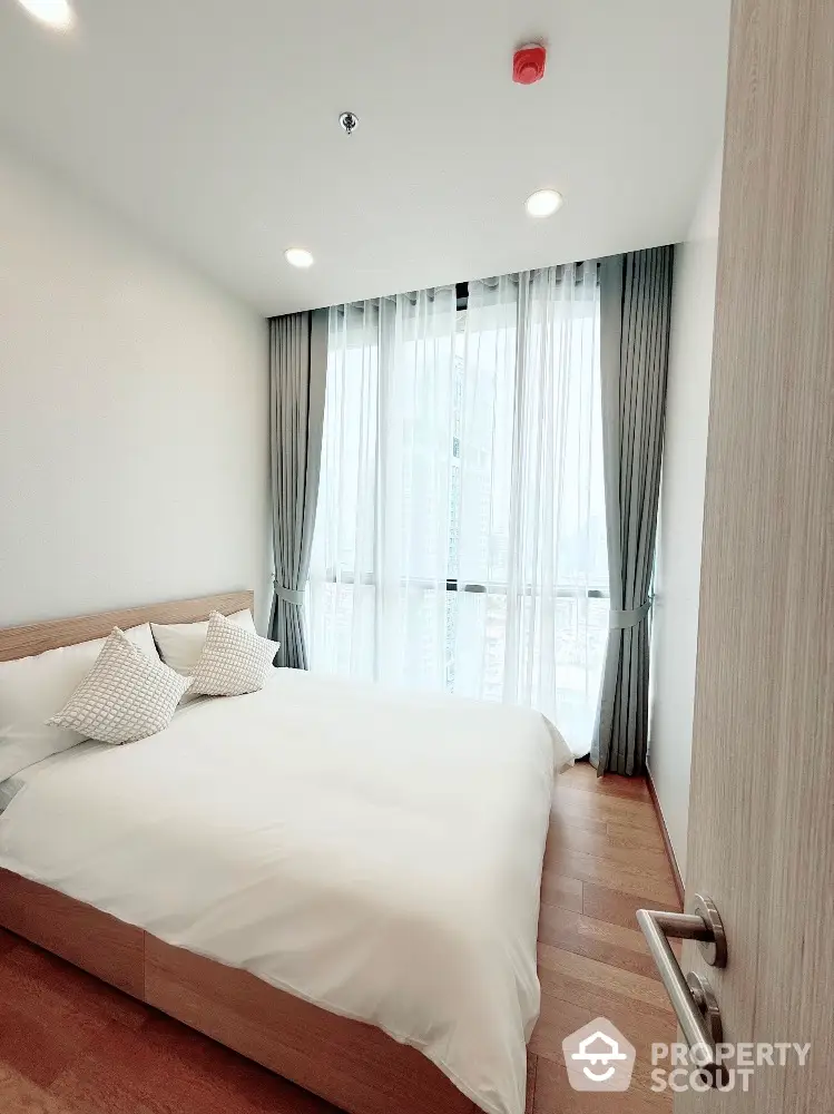 Modern bedroom with large window and minimalist decor in high-rise apartment.