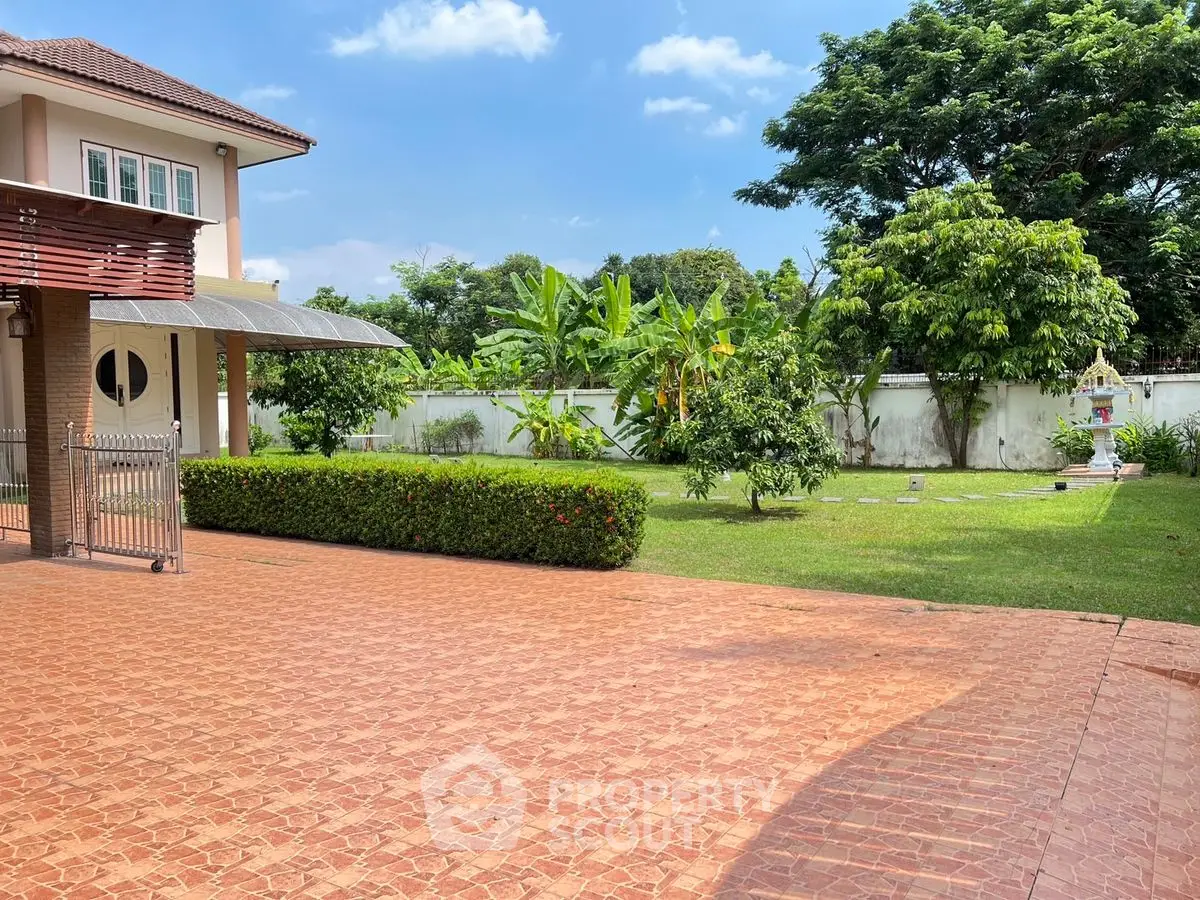 Spacious garden with lush greenery and paved driveway in a serene residential property.