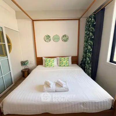 Cozy bedroom with large bed, tropical decor, and ample natural light from window.