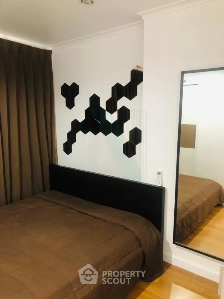 Modern bedroom with stylish decor and mirrored accents, featuring a cozy bed and elegant brown curtains.